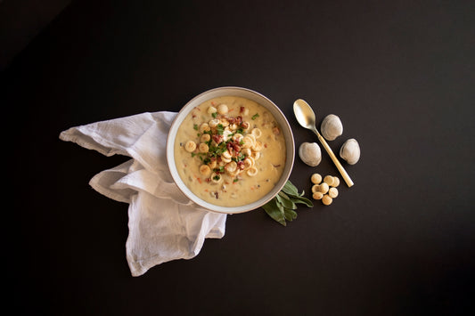 white chowder style soup on black background with spoon, oyster crackers, and clams